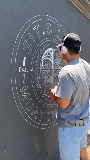 An artist hand-painting the Sit.Silom crest on the gym's outside wall